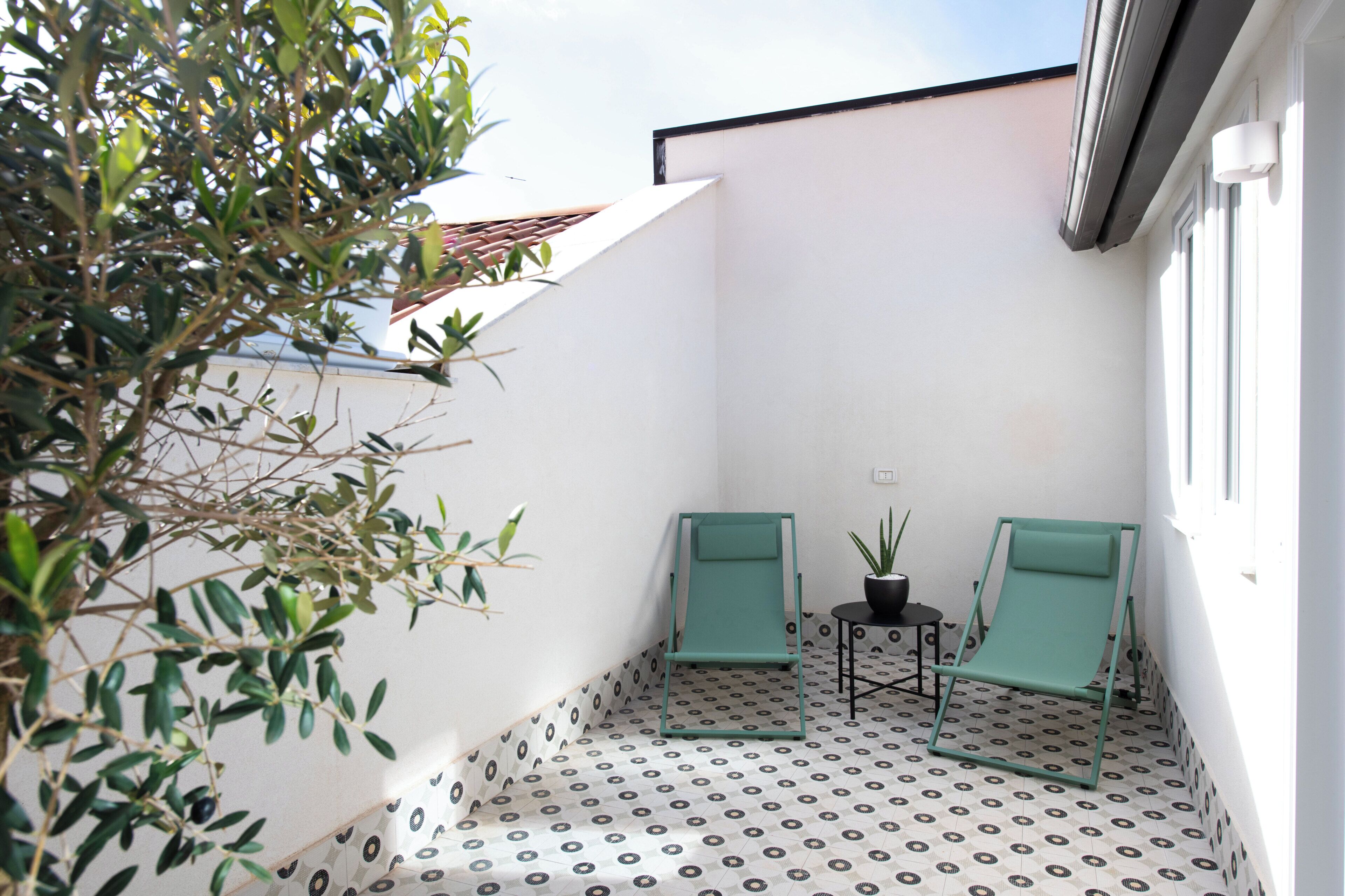 A small outdoor patio with two green chairs, a small table, and a potted plant.