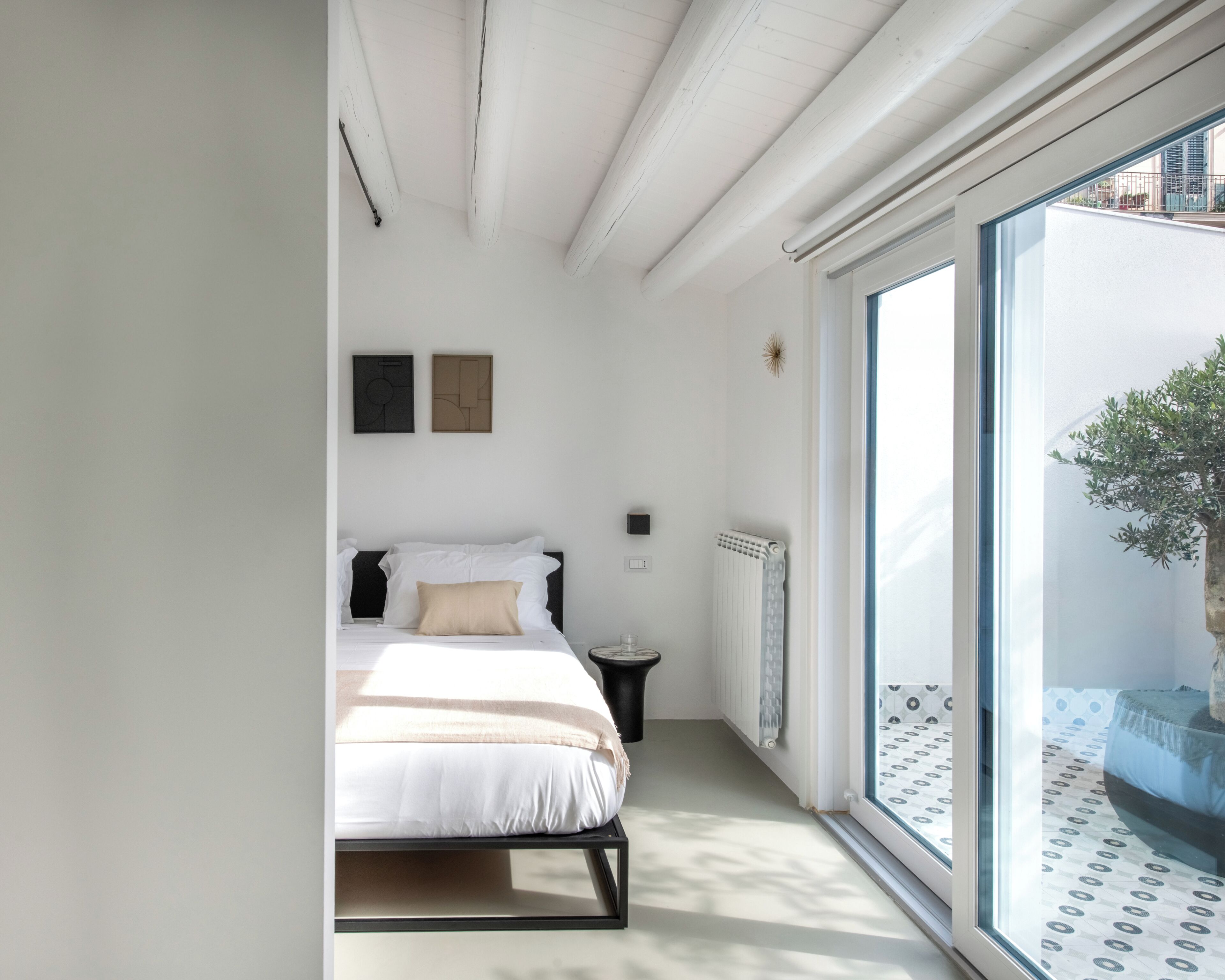 Une chambre à coucher avec un lit, une table de chevet, un radiateur et une vue sur l’extérieur grâce à une grande fenêtre.