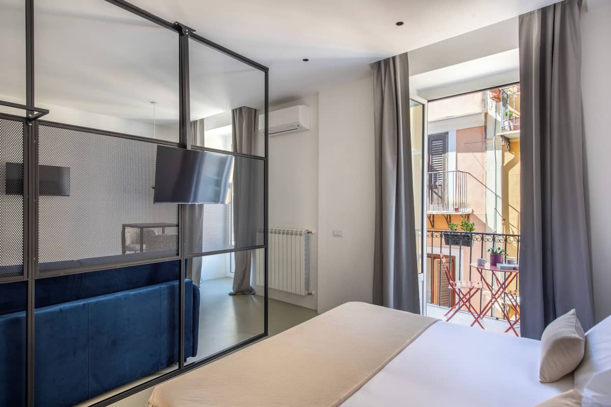 Habitación de hotel con cama, televisión, balcón con mesa y sillas, y vista al exterior.