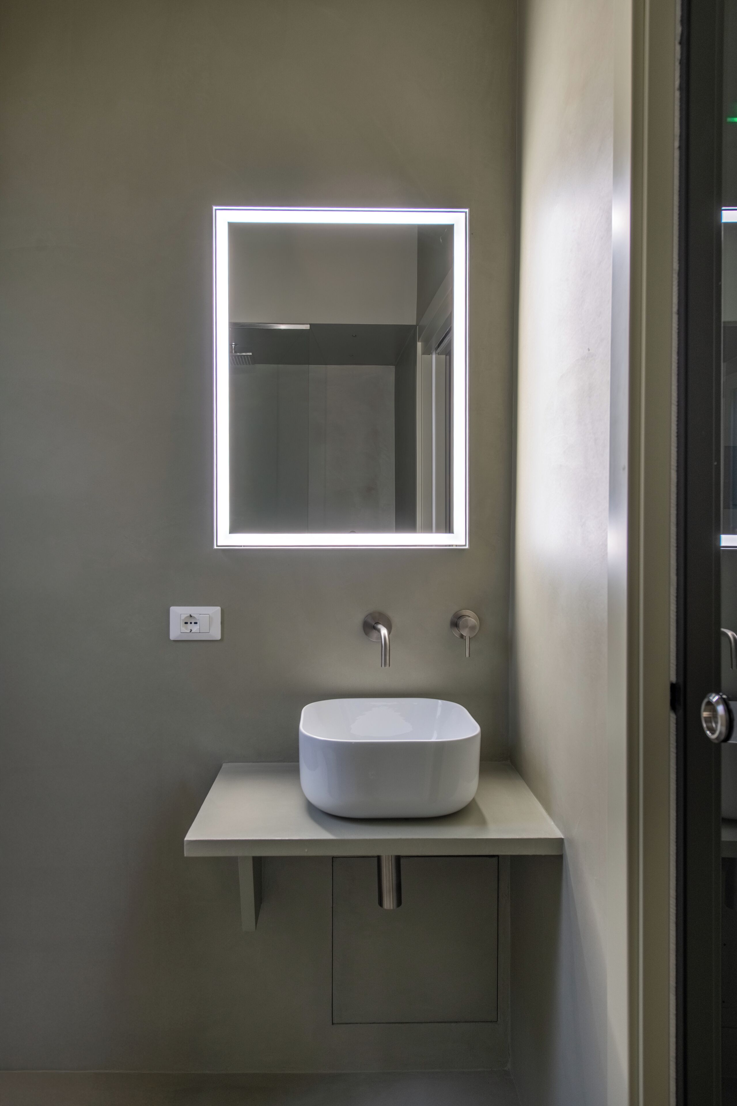 A bathroom with a white sink, a mirror with a light, and a door.