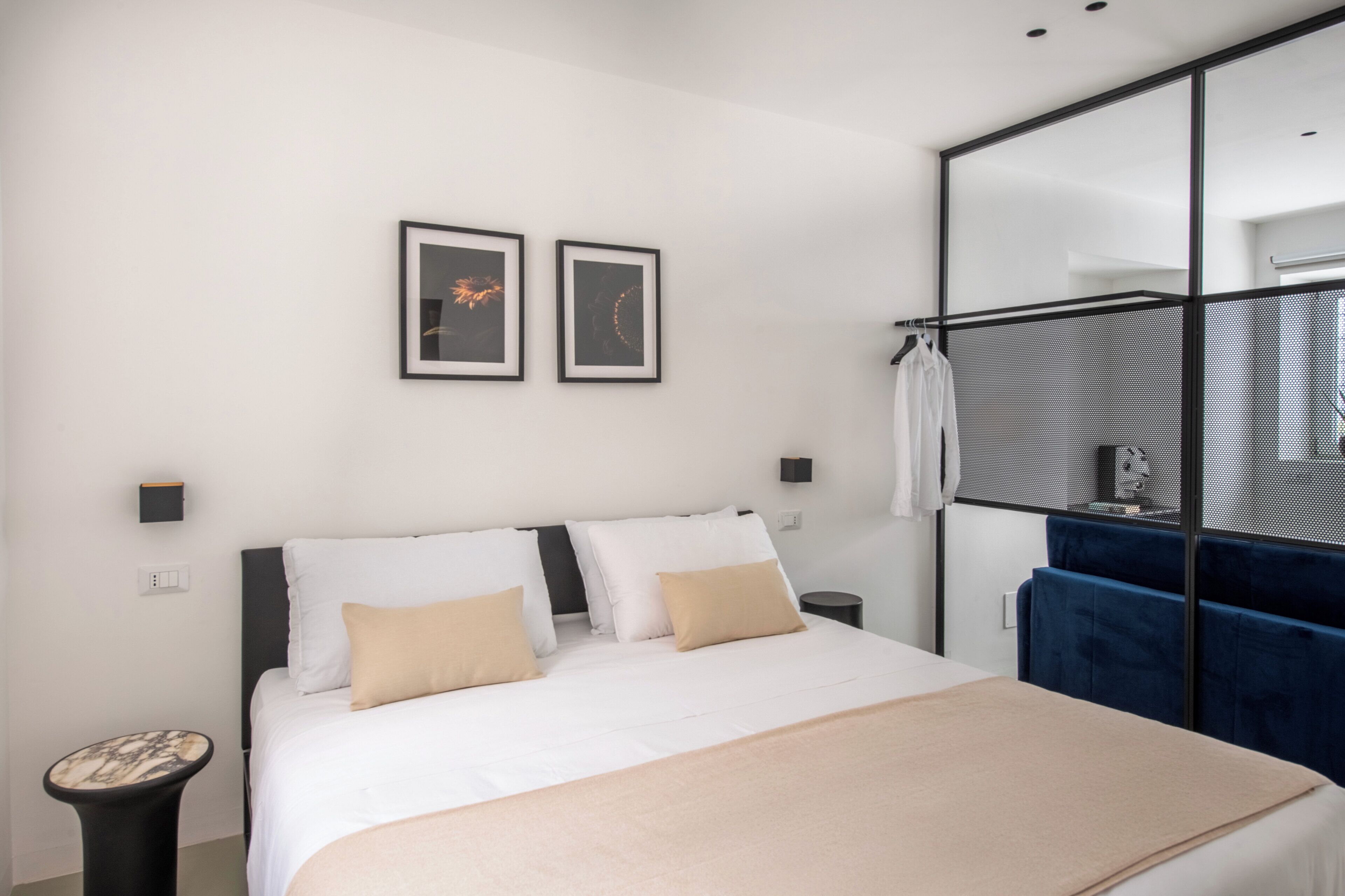 A modern hotel room with a large bed, a wardrobe, a small table, and two framed pictures on the wall.