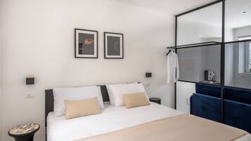 A modern hotel room with a large bed, a wardrobe, a small table, and two framed pictures on the wall.