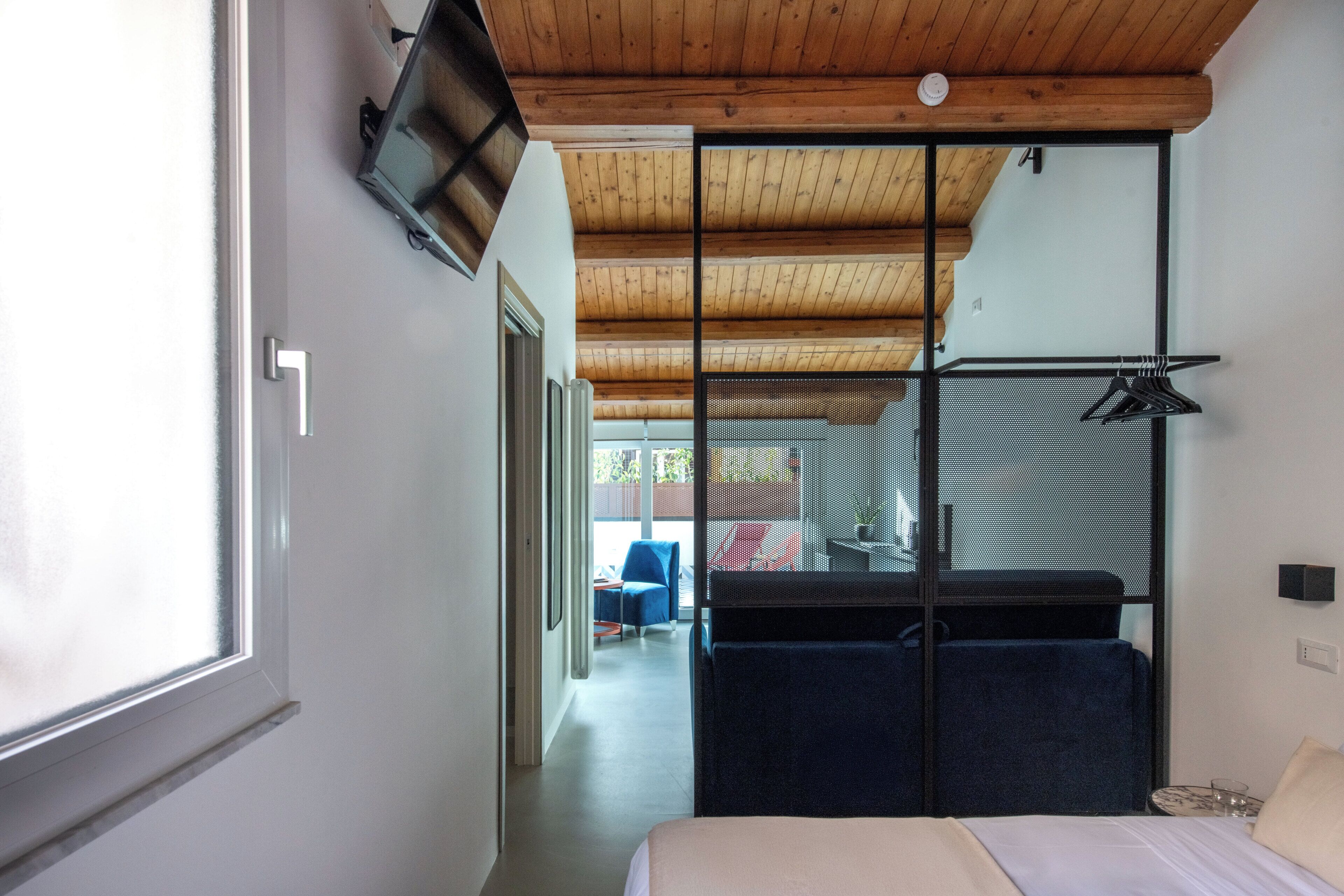 A bedroom with a bed, a TV mounted on the wall, and a sliding door leading to a balcony.