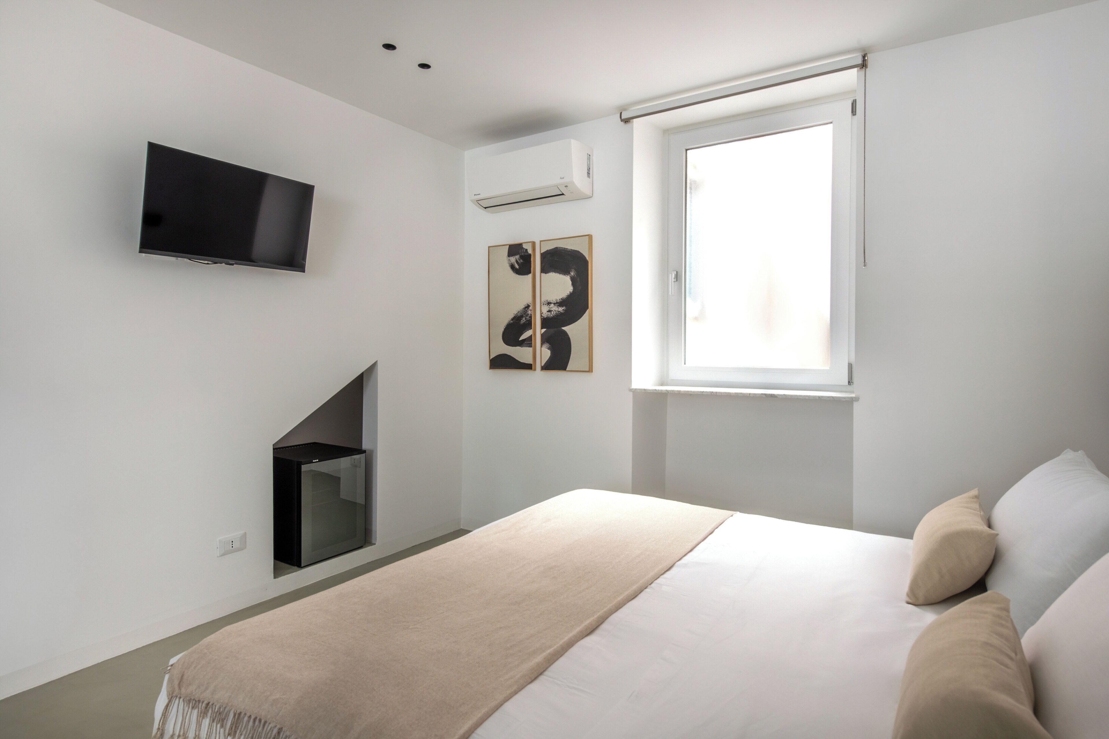 A modern bedroom with a bed, a TV mounted on the wall, and a window.