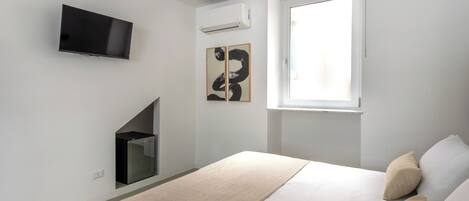 Un dormitorio moderno con una cama, un televisor montado en la pared y una ventana.