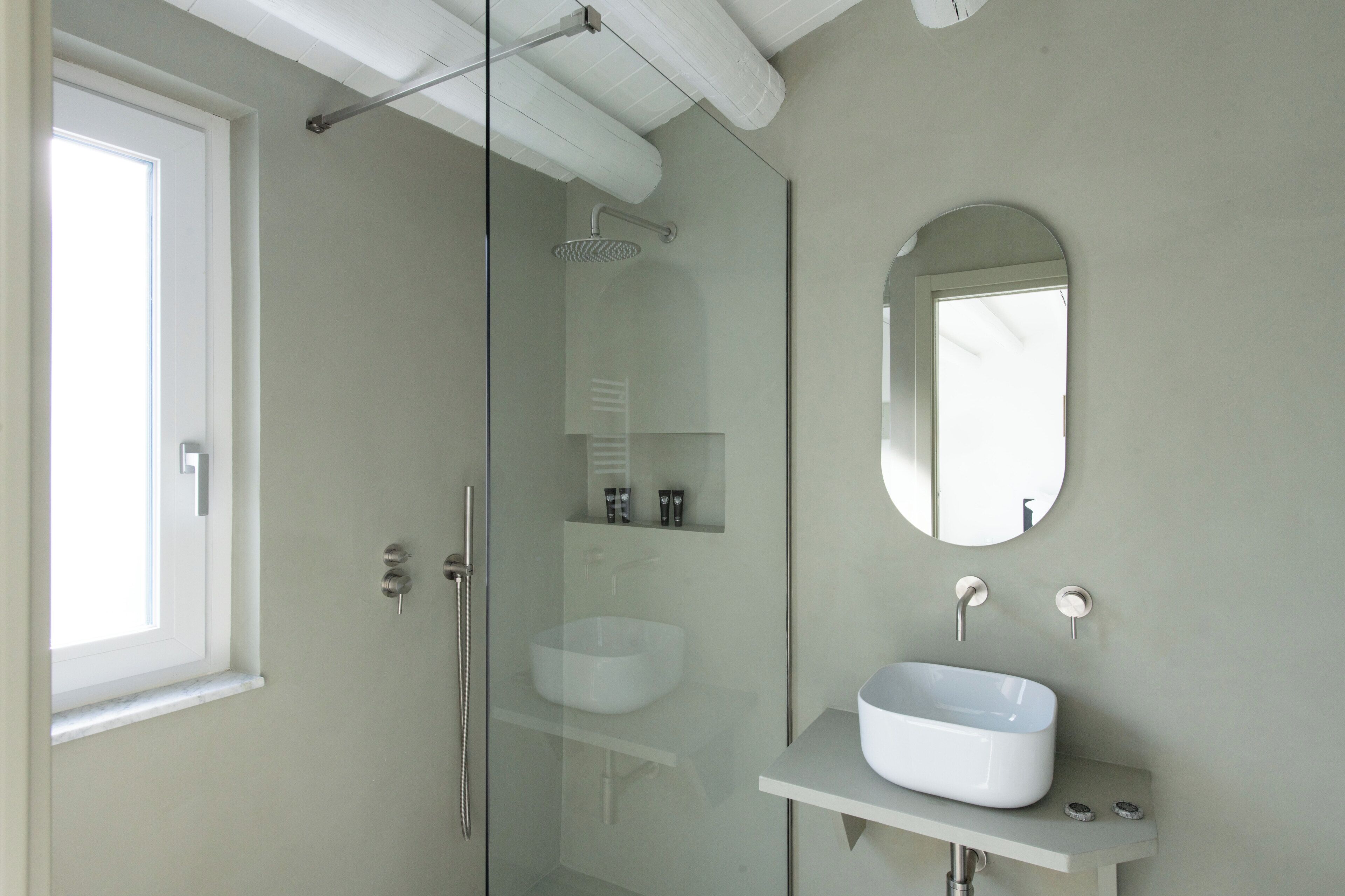 A modern bathroom with a glass shower enclosure, a white sink, and a mirror on the wall.
