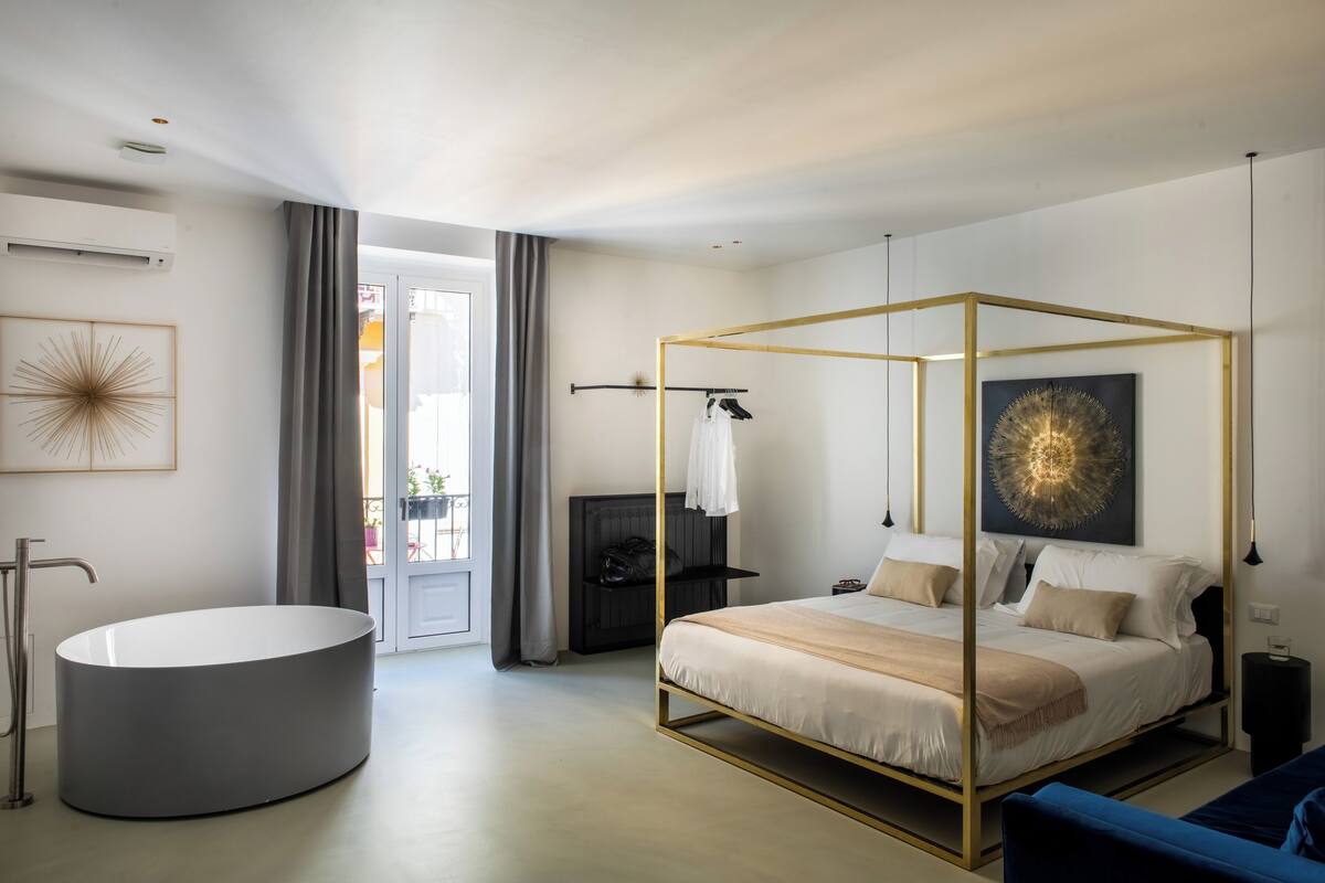 Un dormitorio moderno con cama con dosel, bañera redonda y ventana grande.