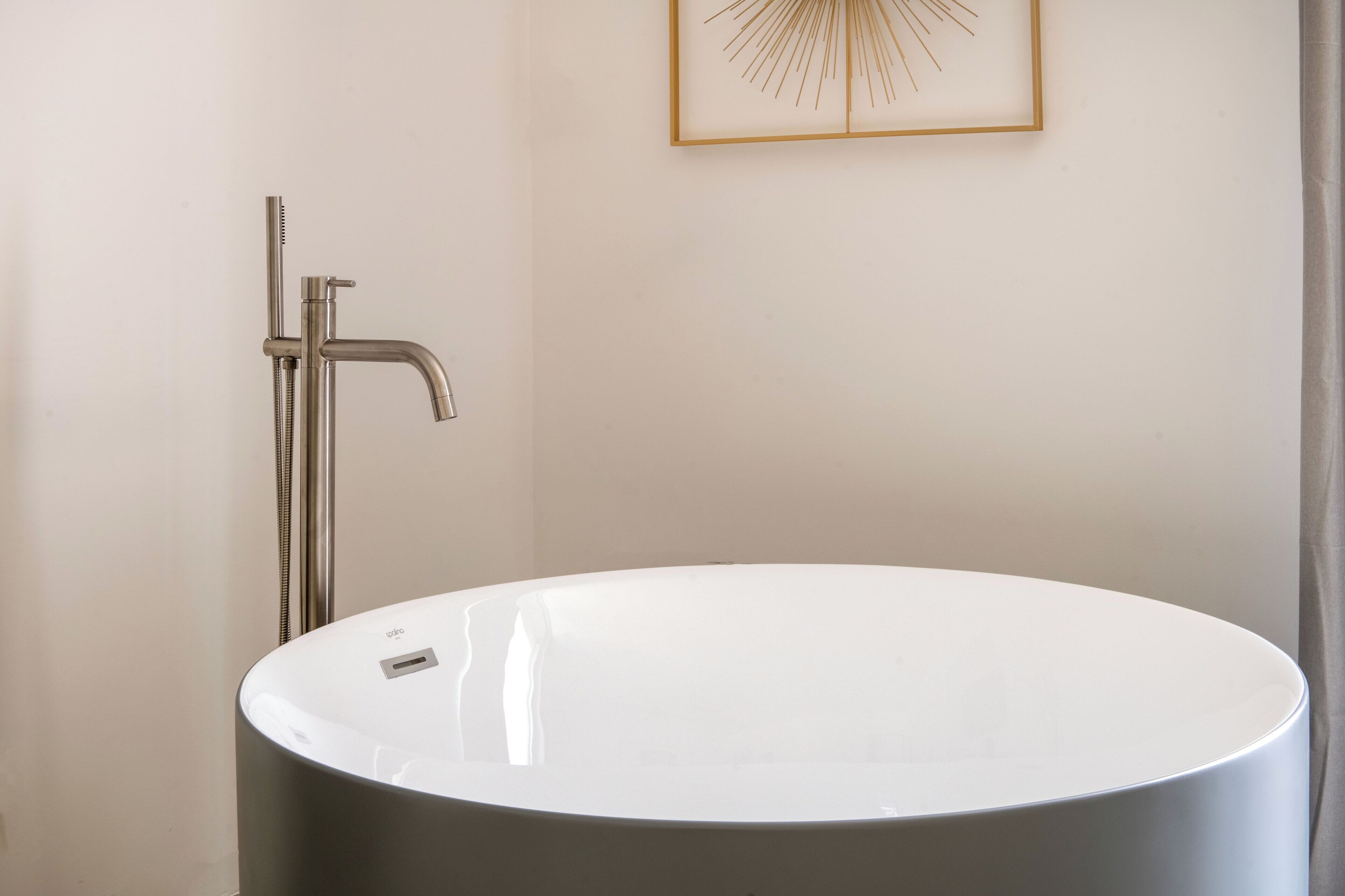 A modern bathroom with a round bathtub, a shower with a handheld showerhead, and a framed artwork on the wall.