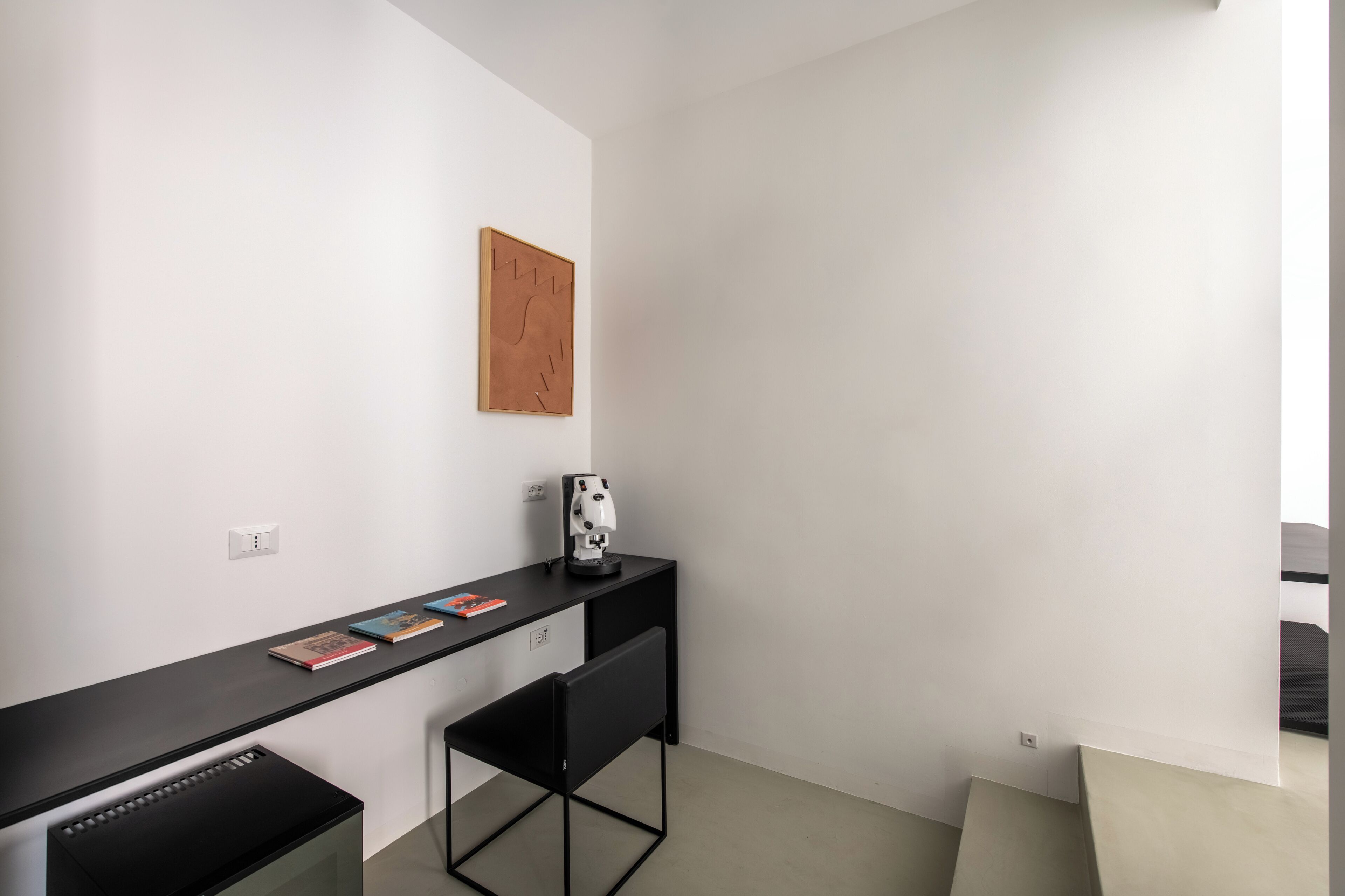 Una habitación pequeña y moderna con escritorio, silla e imagen colgada en la pared.