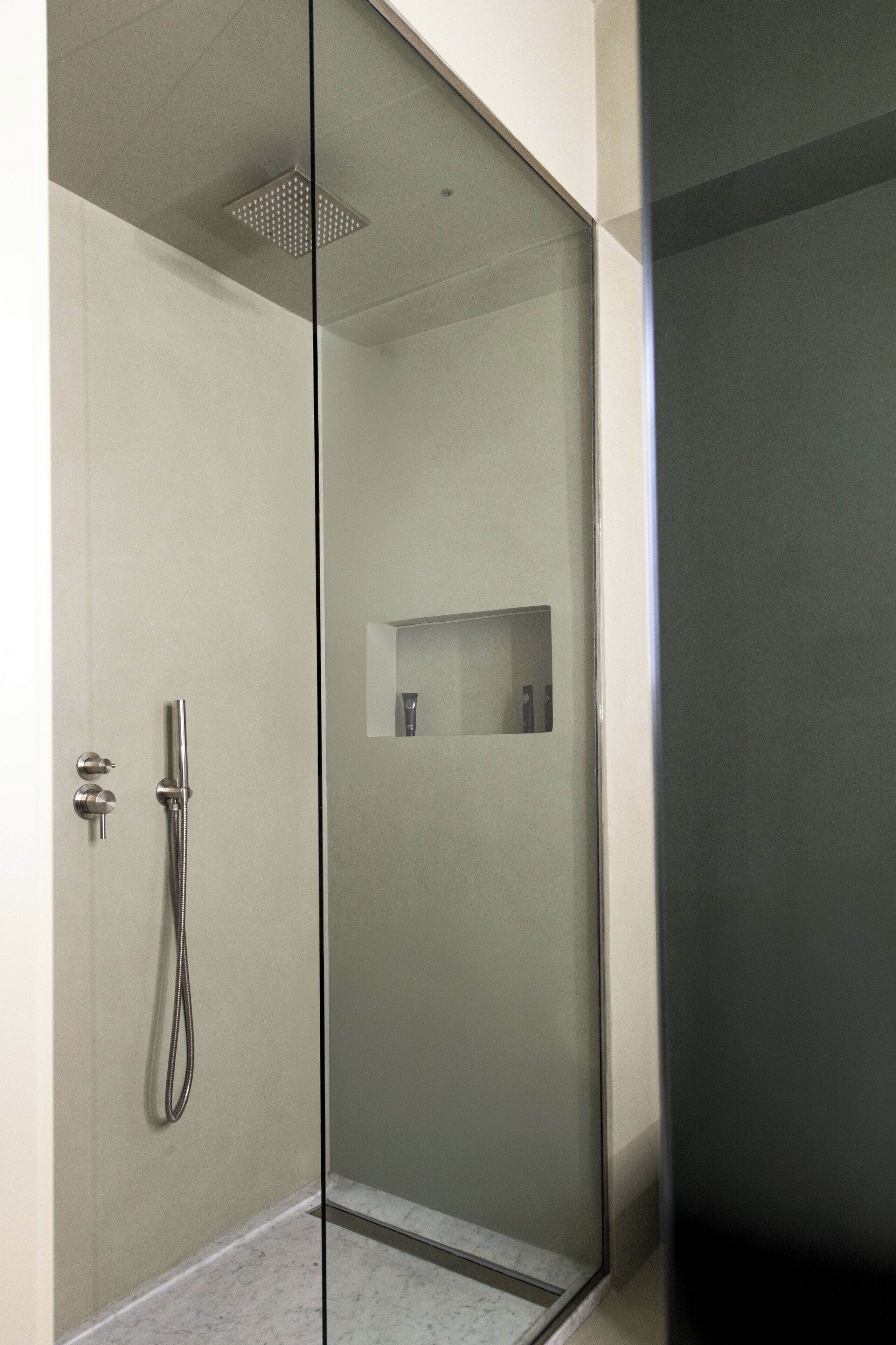 A modern shower with a glass door, a handheld showerhead, and a small shelf with toiletries.