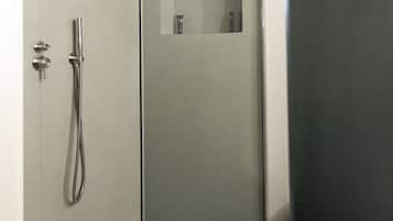 A modern shower with a glass door, a handheld showerhead, and a small shelf with toiletries.
