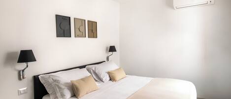 A hotel room with a bed, wall-mounted artwork, two bedside lamps, and an air conditioning unit.