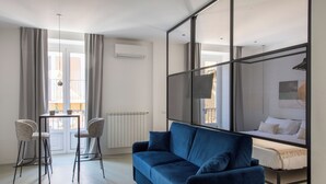 A modern room with a blue sofa, two chairs, a small table, a bed with a privacy screen, and a view of the outside. - Palazzo Achates (Palermo)
