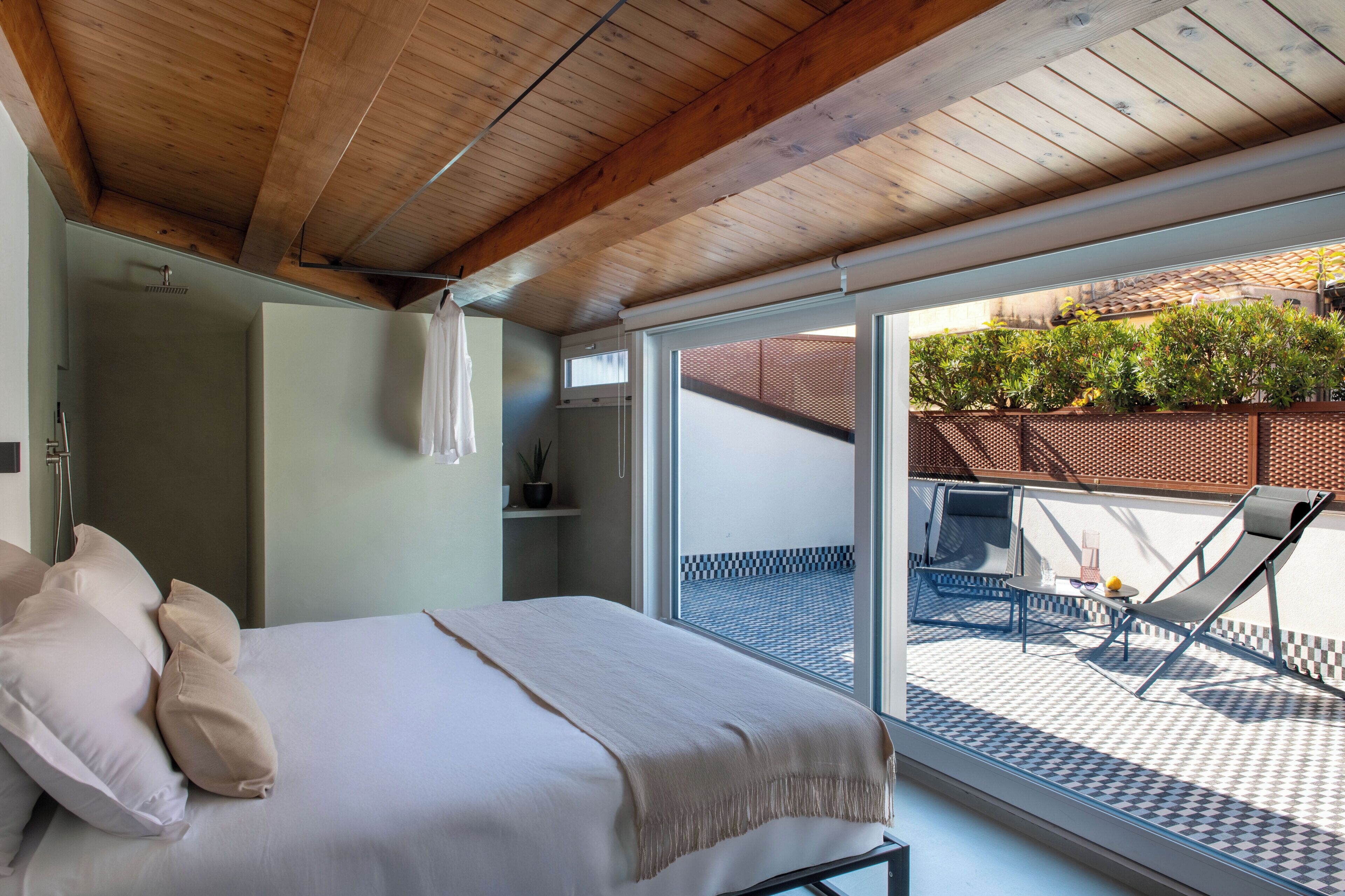 Een slaapkamer met een bed, een douche en een balkon met een tafel en stoelen.