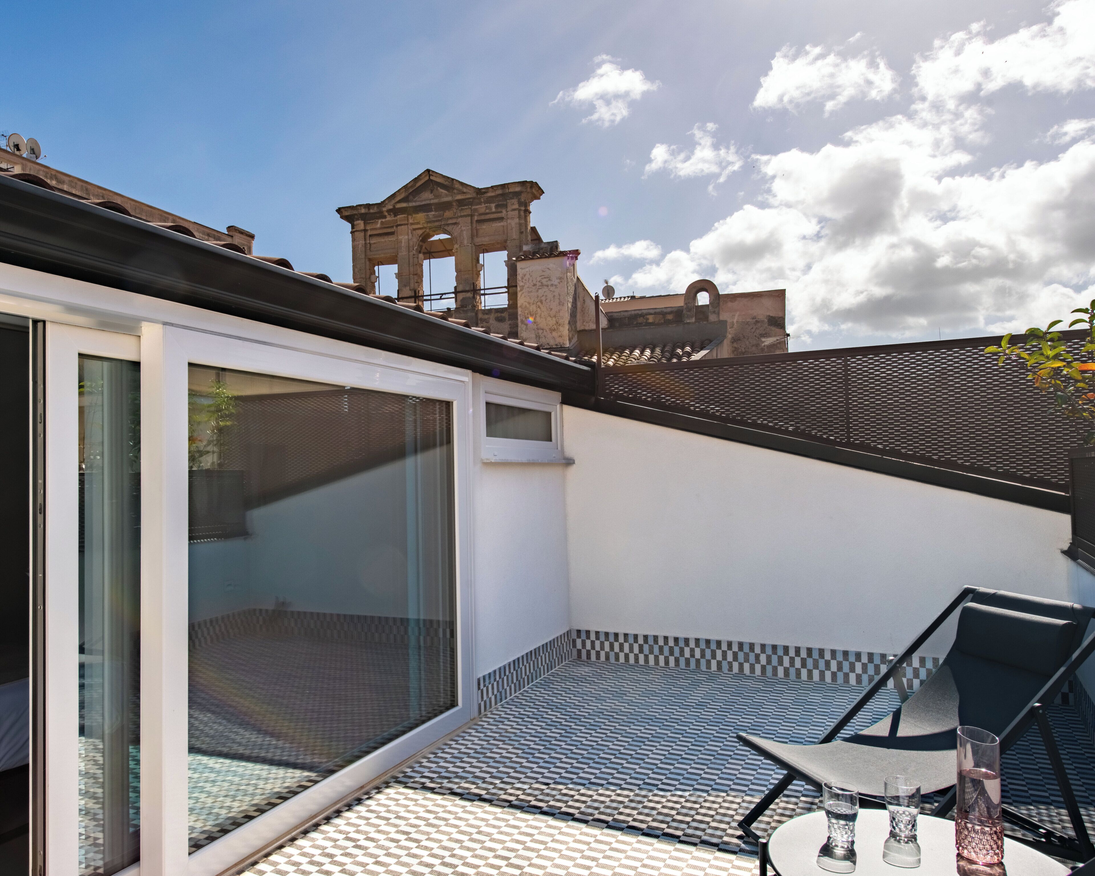 A modern patio with a glass door, a tiled floor, and a view of historical architecture in the background.
