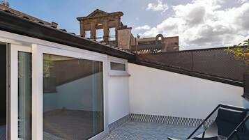 A modern patio with a glass door, a tiled floor, and a view of historical architecture in the background.