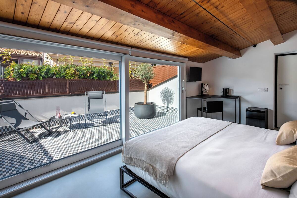 Un dormitorio con una cama grande, vistas a un patio con mesa y sillas, una planta en maceta y un televisor en la pared.