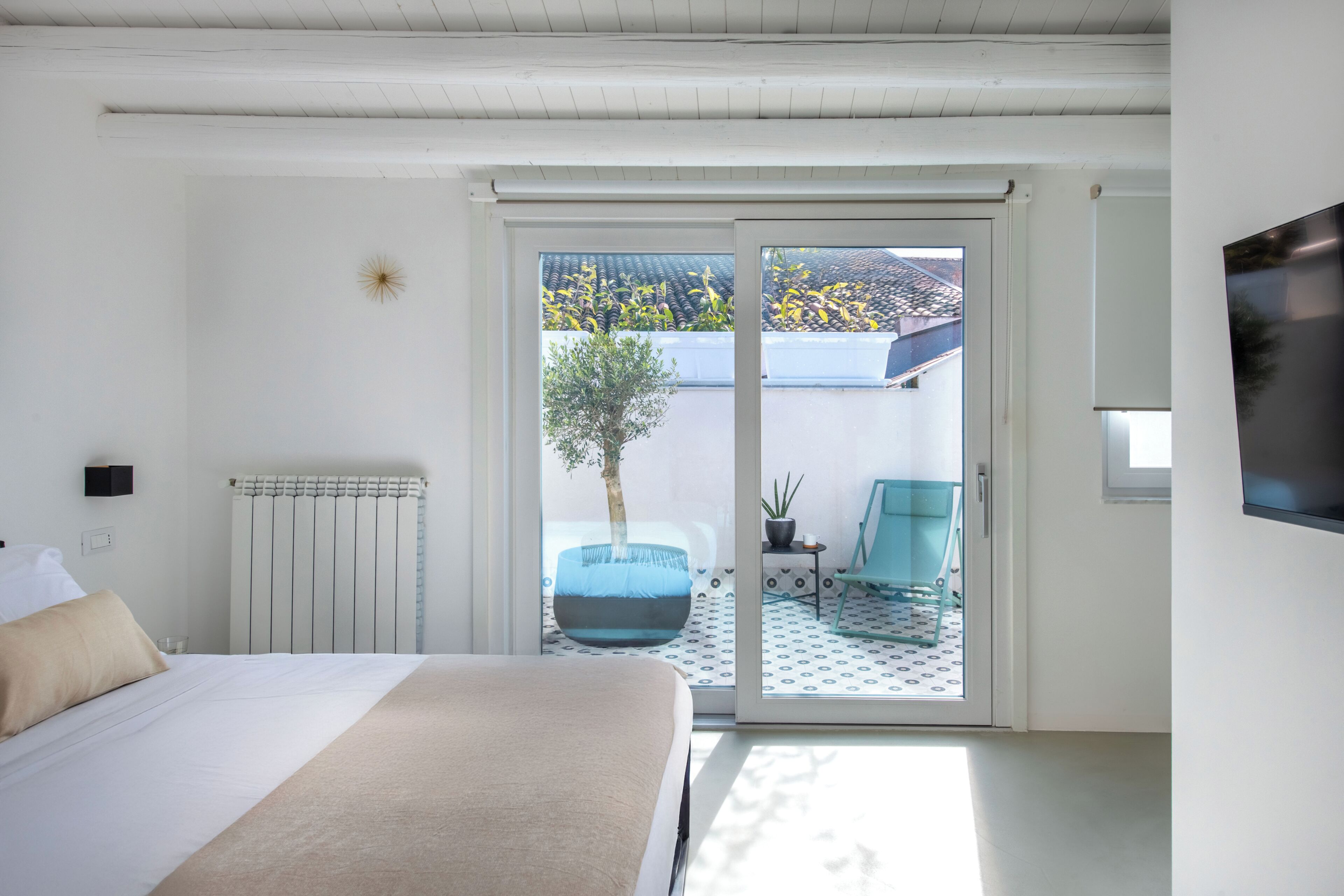 Een slaapkamer met een bed, een schuifdeur naar een buitenruimte, een aan de muur bevestigde televisie en een kleine tafel met een plant.