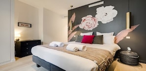 Une chambre à coucher moderne avec un grand lit, une table de chevet, une lampe fixée au mur et un élément décoratif mural.