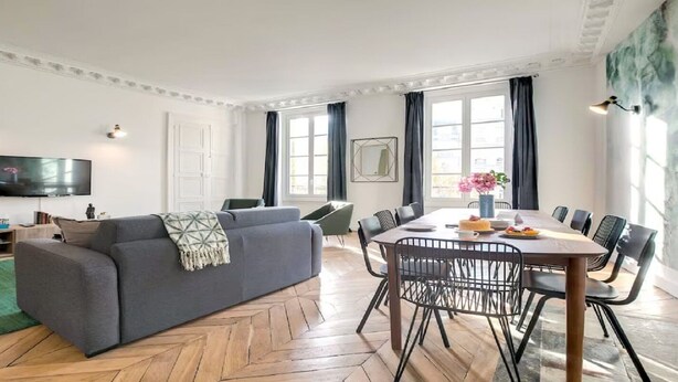A modern living room with a sofa, dining table, chairs, a TV, and a green rug. - Bonne Nouvelle Beauty | 200m² of Parisian Elegance Near Opéra (Paris)