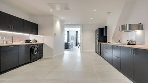 A modern kitchen with dark cabinetry, a washing machine, and a countertop with various appliances. - Bonne Nouvelle Beauty | 200m² of Parisian Elegance Near Opéra (Paris)