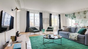 A modern living room with a flat-screen TV, two armchairs, a sofa, a coffee table, and a green rug. - Bonne Nouvelle Beauty | 200m² of Parisian Elegance Near Opéra (Paris)