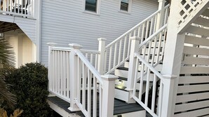 A two-story house with a white exterior, a wooden staircase with white railings, and a small balcony. - Fabulous 4-bedroom channel home with private dock in Cherry Grove Beach. (North Myrtle Beach)