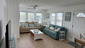 A living room with a beige sofa, teal sofa, white coffee table, and a ceiling fan. - Fabulous 4-bedroom channel home with private dock in Cherry Grove Beach. (North Myrtle Beach)