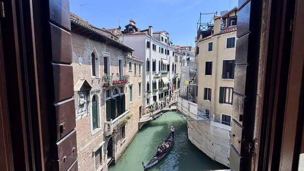 A narrow canal with a gondola, flanked by historic buildings with balconies and windows. - Angelo Prestige Canal View (Venice)