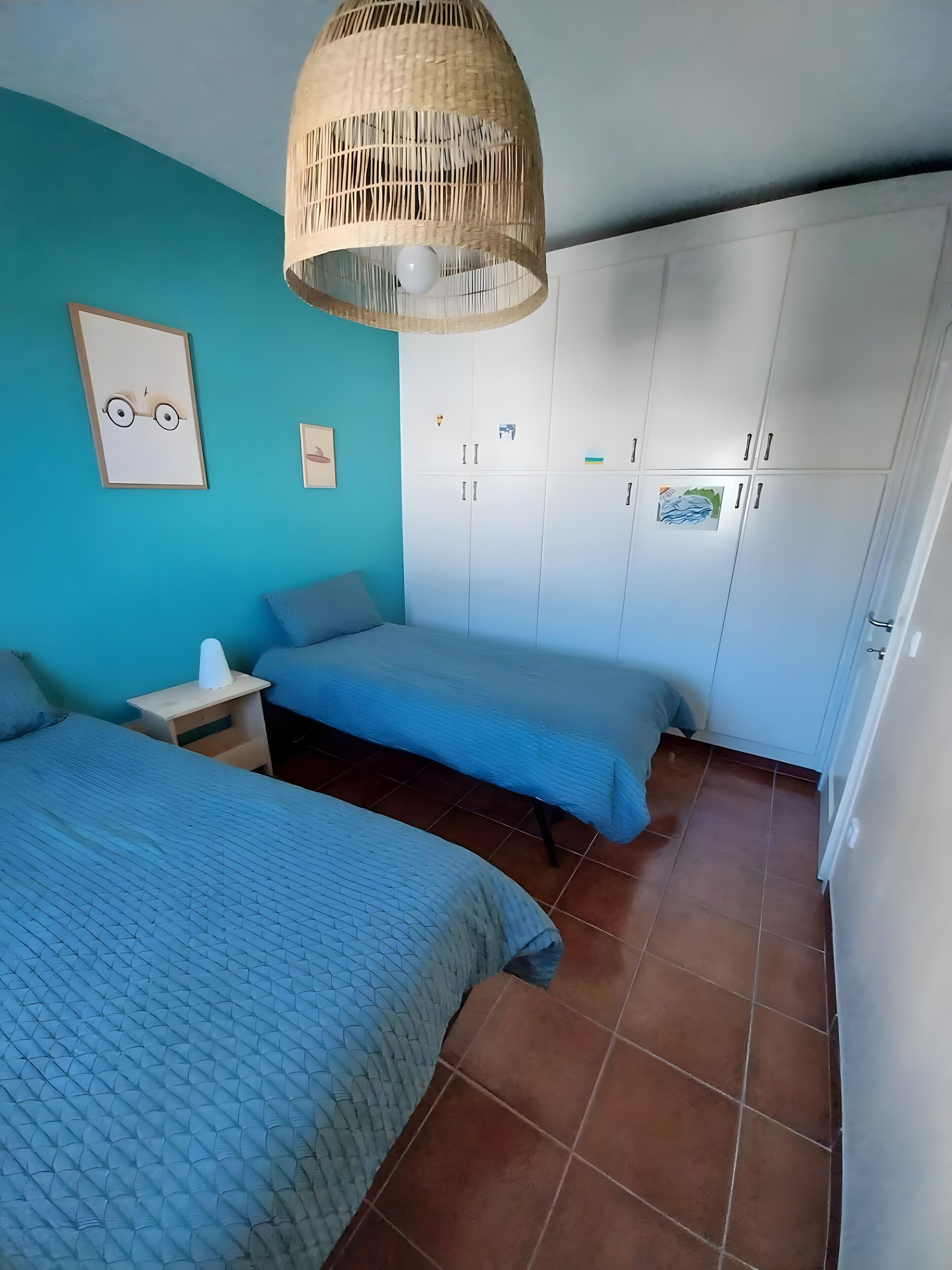 A room with two beds, a wardrobe, a hanging light fixture, and a wall clock.