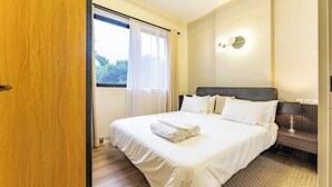 Une chambre d’hôtel avec un lit, une table de chevet, une lampe et une fenêtre avec des rideaux.