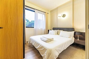 A hotel room with a bed, a nightstand, a lamp, and a window with curtains. - Kilimani, Wilma Tower, Studio, Steam, Sauna, Pool &Gym (Nairobi)