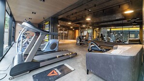 Une salle de sport équipée de tapis de course, de vélos elliptiques et d’un fauteuil de massage.