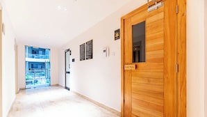 Un couloir avec une porte en bois portant l’inscription « SAUNA », une porte en verre donnant sur un espace extérieur et un panneau fixé au mur.