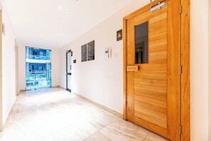 A hallway with a wooden door labeled 'SAUNA,' a glass door leading to an outdoor area, and a wall-mounted sign. - Kilimani, Wilma Tower, Studio, Steam, Sauna, Pool &Gym (Nairobi)
