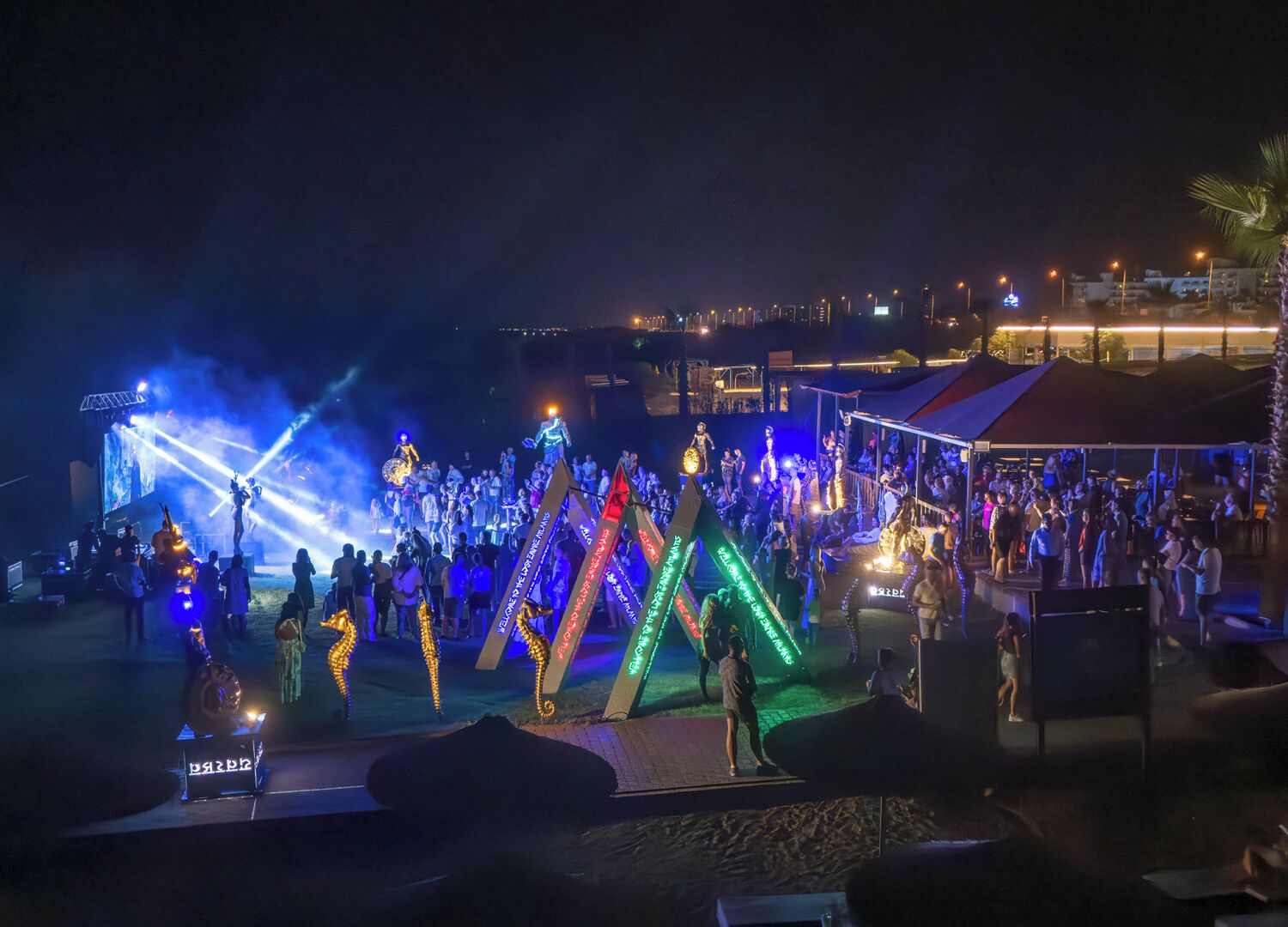 Evento noturno ao ar livre com palco, estruturas iluminadas e uma multidão.