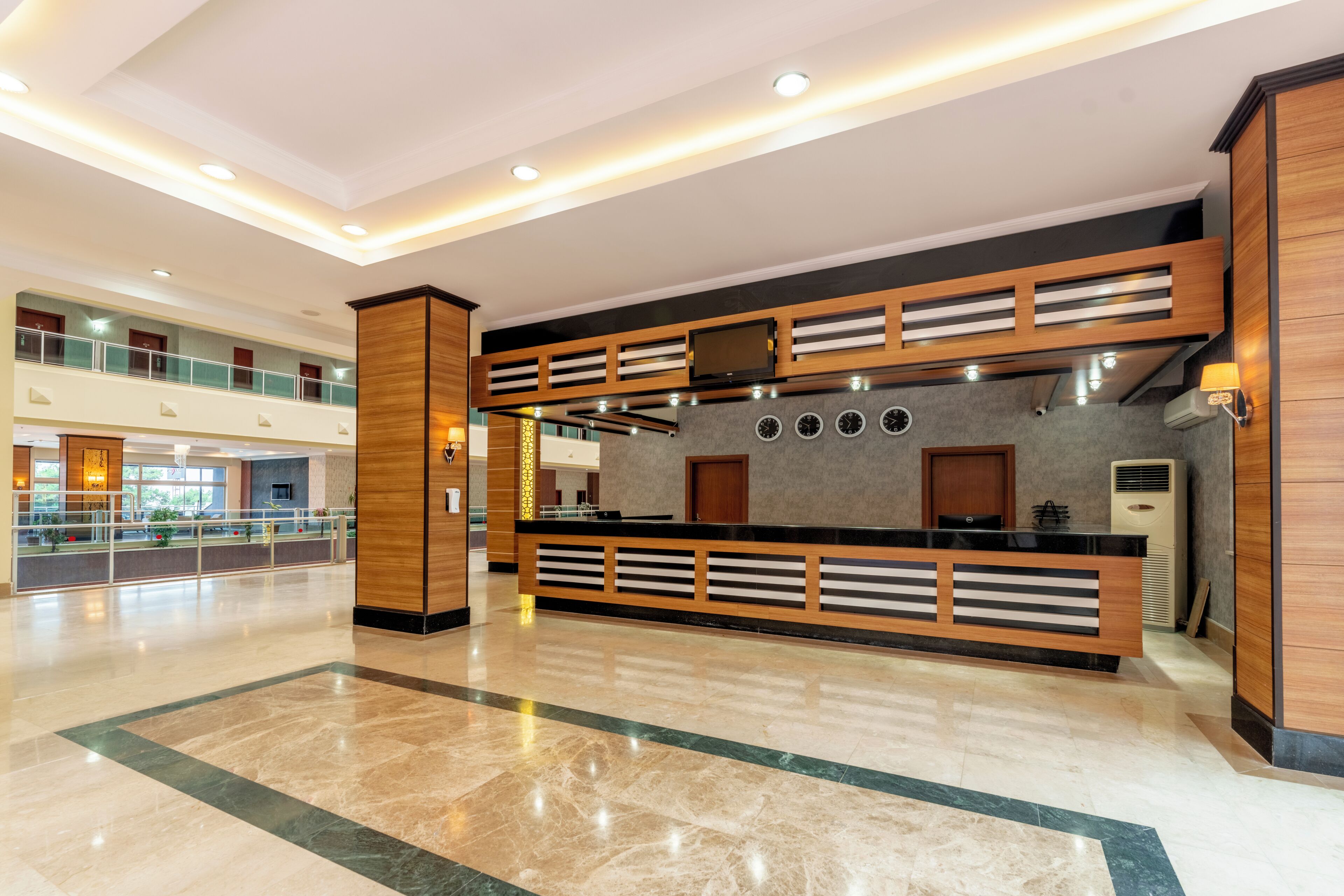 A modern hotel lobby with a reception desk, a second-floor balcony, and a marble floor.