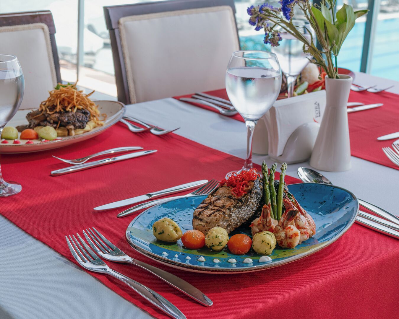 A dining table with plates of food, cutlery, and a vase with flowers.