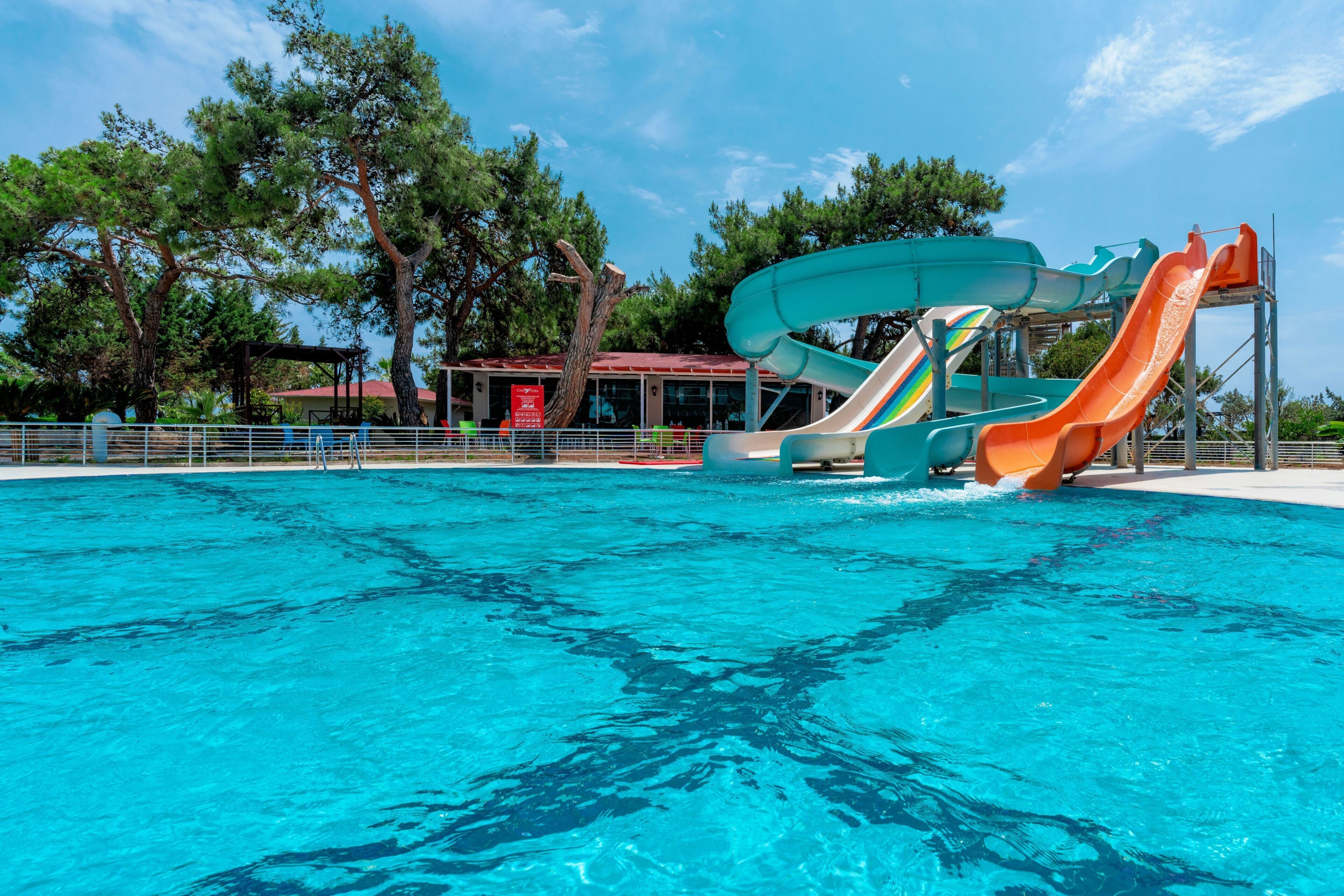Una piscina con varias toboganes, rodeada de árboles y un edificio de techo rojo.