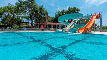 Una piscina con varias toboganes, rodeada de árboles y un edificio de techo rojo.