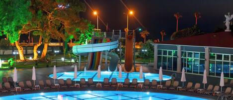 A swimming pool with a slide, lounge chairs, and a building with large windows in the background.