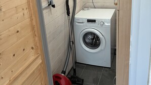 A compact laundry room with a Bosch washing machine, a red vacuum cleaner, and wooden panel walls. - Private vacation home with large terrace & garden - quiet location near Bodden/Baltic Sea (Saal)
