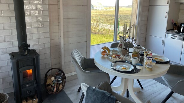A cozy kitchen with a wood-burning stove, a dining table with breakfast items, and a view of the countryside. - Private vacation home with large terrace & garden - quiet location near Bodden/Baltic Sea (Saal)