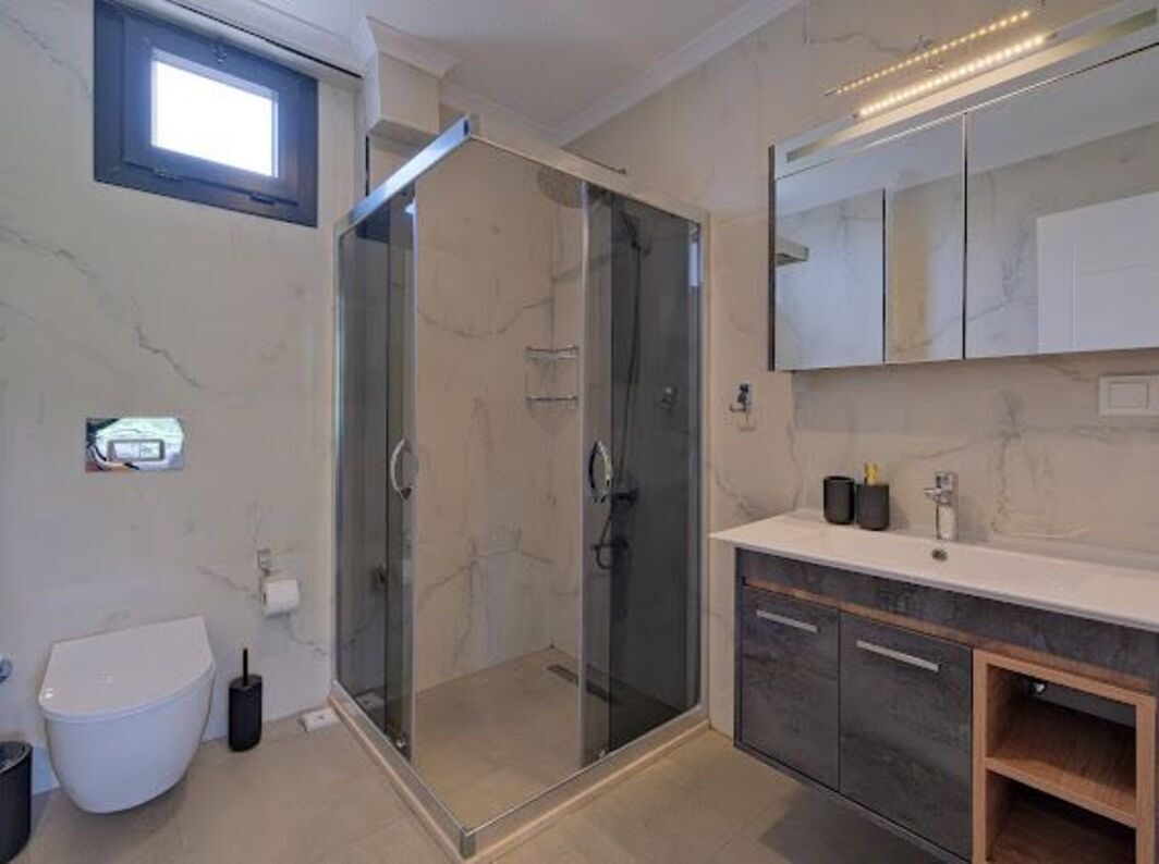 Een moderne badkamer met een douchecabine van glas, een toilet, een wastafel met spiegel en een marmeren wand.