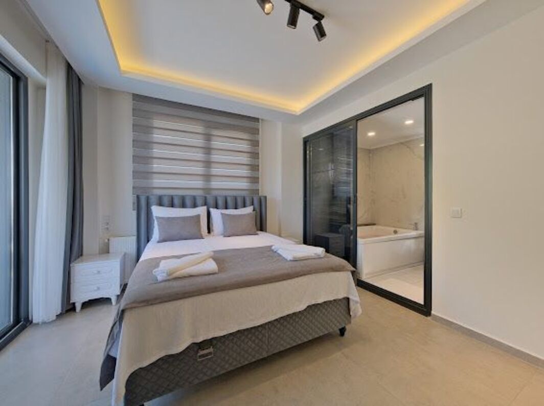 Ein modernes Schlafzimmer mit einem großen Bett, Nachttischen, einer Duschkabine aus Glas und Blick durch die Glastür.