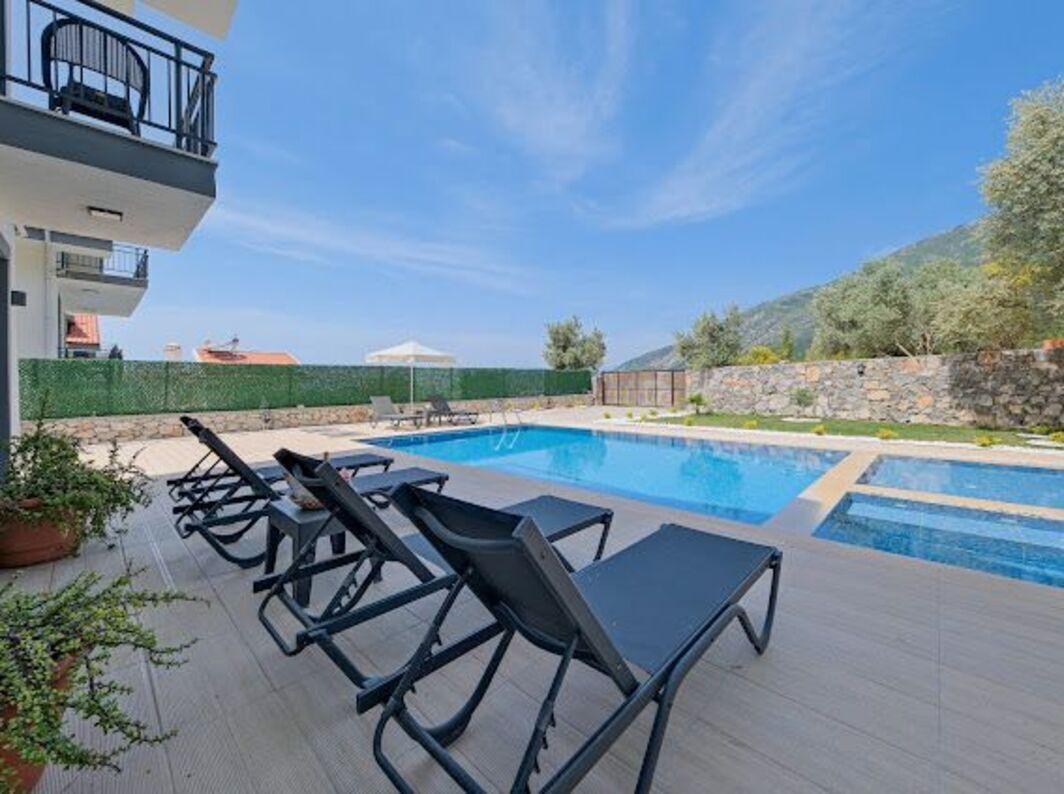 A swimming pool with lounge chairs, a stone wall, and a building with balconies.