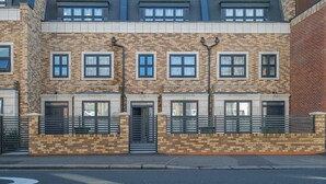 A row of modern brick townhouses with uniform window designs and a central entrance. - 4BDR 3BA Family Home Garden in Isleworth (Isleworth)