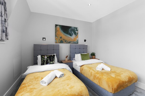 A hotel room with two beds, each with a headboard, a painting on the wall, and a small table with a plant. - 4BDR 3BA Family Home Garden in Isleworth (Isleworth)