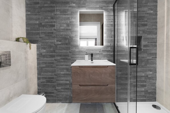 A modern bathroom with a glass shower enclosure, a wooden vanity, and a large mirror.