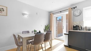 A modern kitchen with a dining area, a clock, and a sliding door to a balcony. - 4BDR 3BA Family Home Garden in Isleworth (Isleworth)